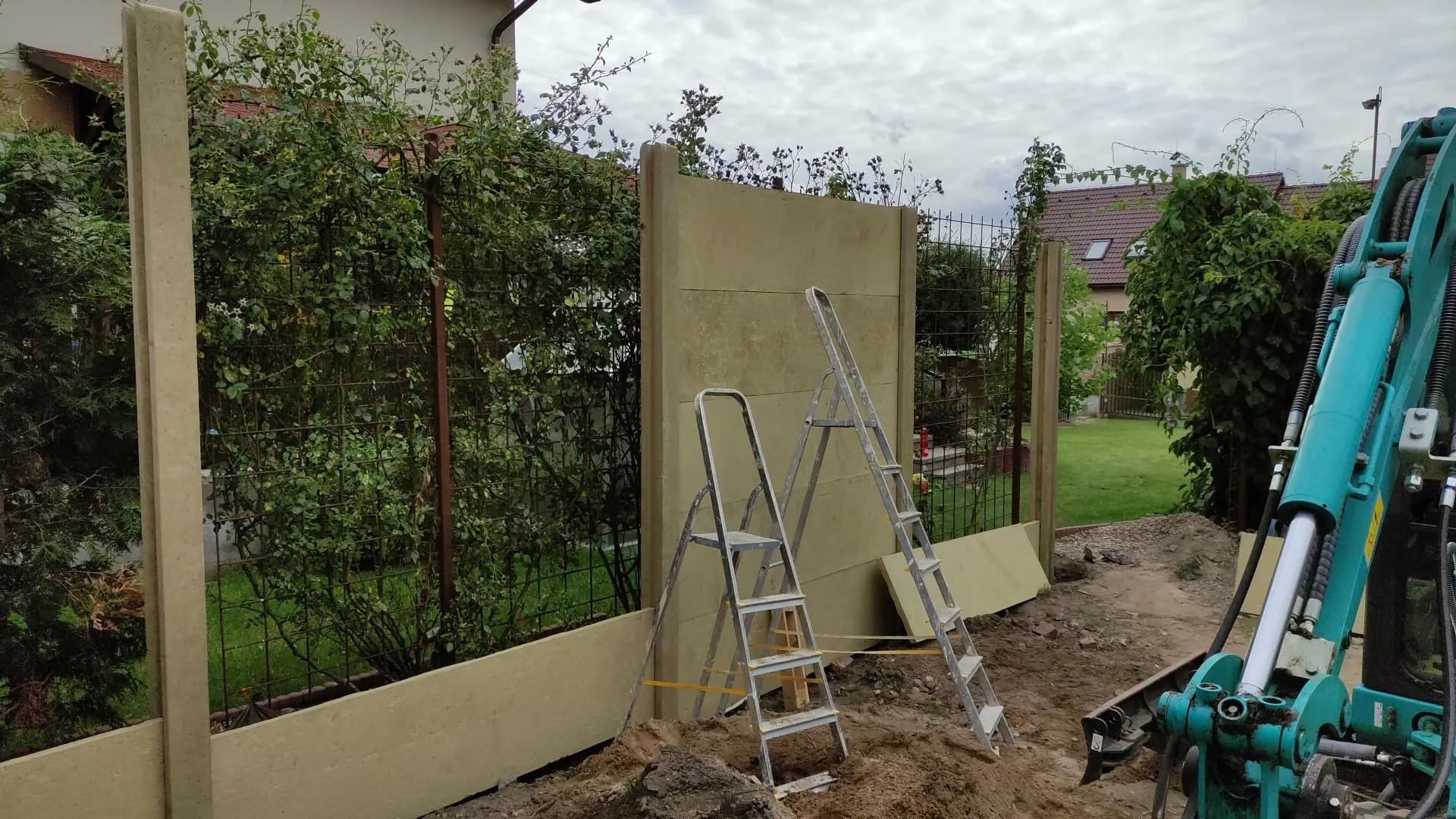 Osazování betonového plotu na zahradě s pomocí minibagru
