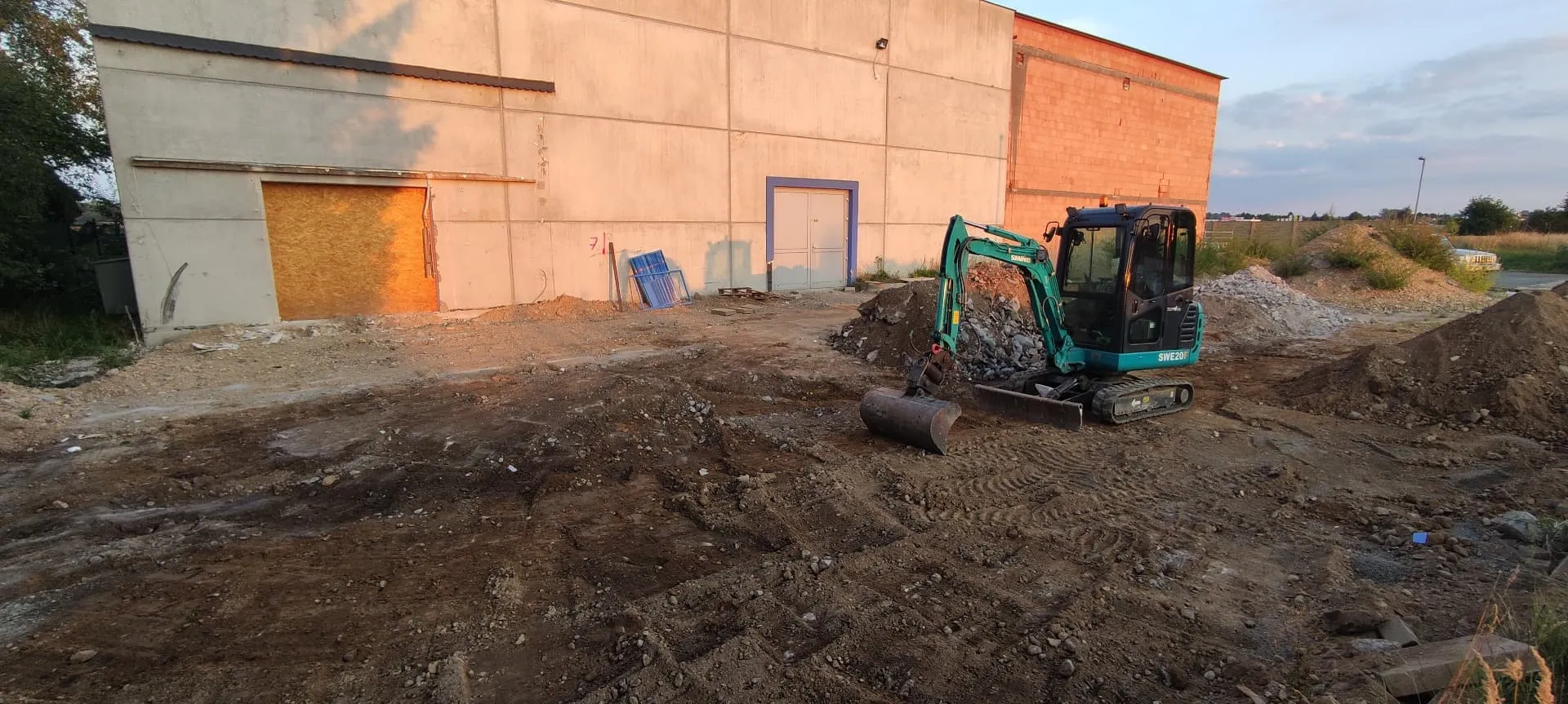 Minibagr při odstraňování betonu a přípravě plochy u průmyslové haly