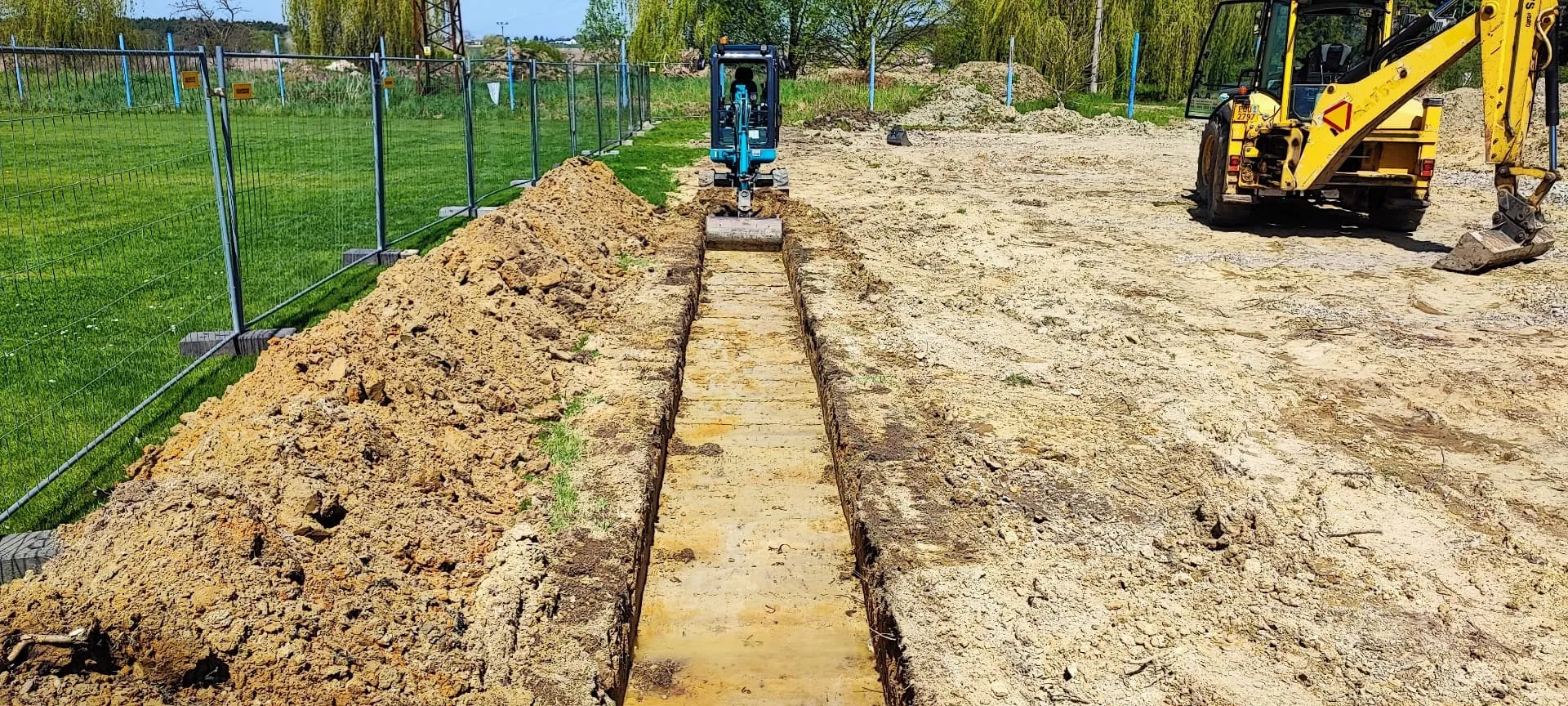 Minibagr hloubí přesnou rýhu pro základové pásy na stavebním pozemku