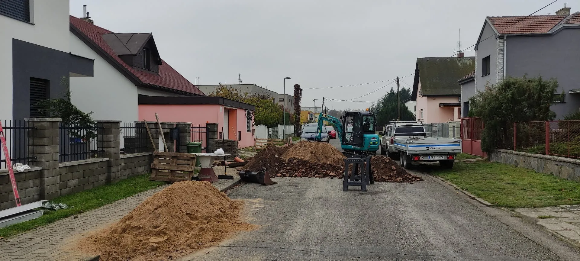 Minibagr při výkopu pro přípojku v ulici rodinných domů