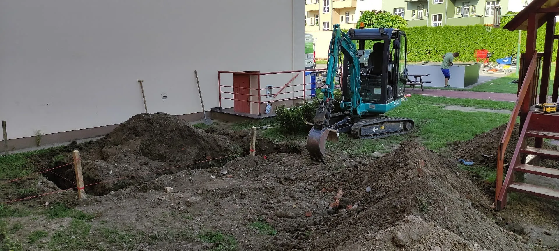 Minibagr hloubí vytyčené základy u bytového domu